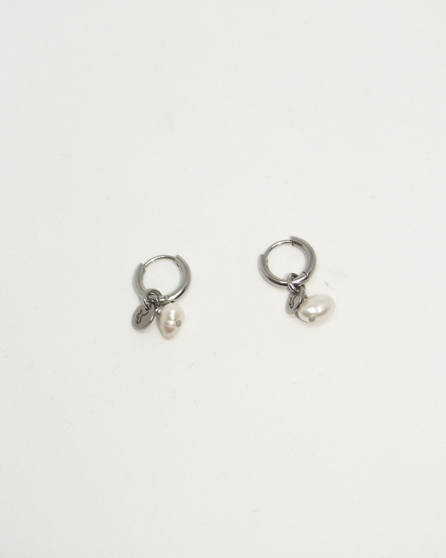 Pair of silver hoop earrings with small round pendants on a light gray background