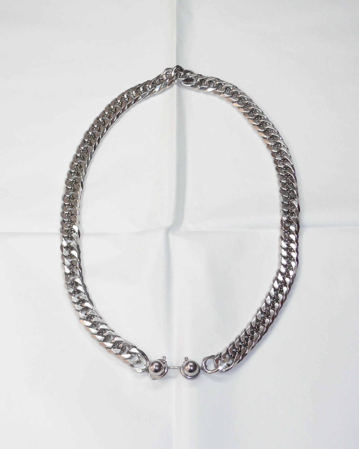 Chunky silver chain necklace with piercing closure on folded paper