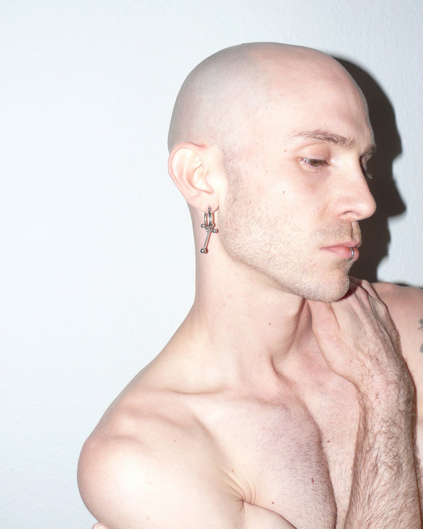 Cross shaped steel barbell hoop earrings portrait on model touching shoulder