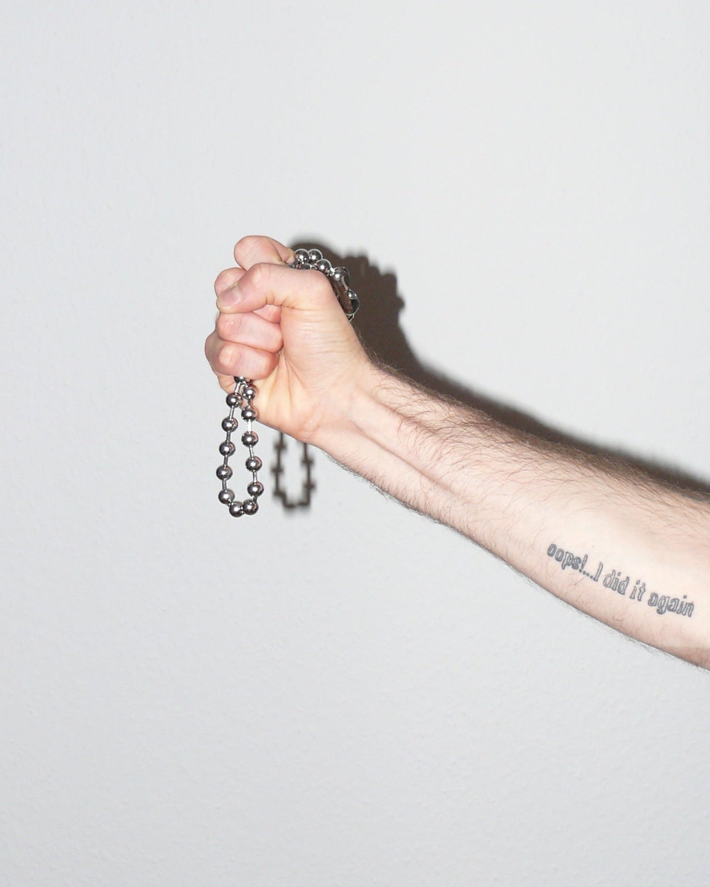 Hand holding a metal chain with a tattoo on the arm against a light gray background