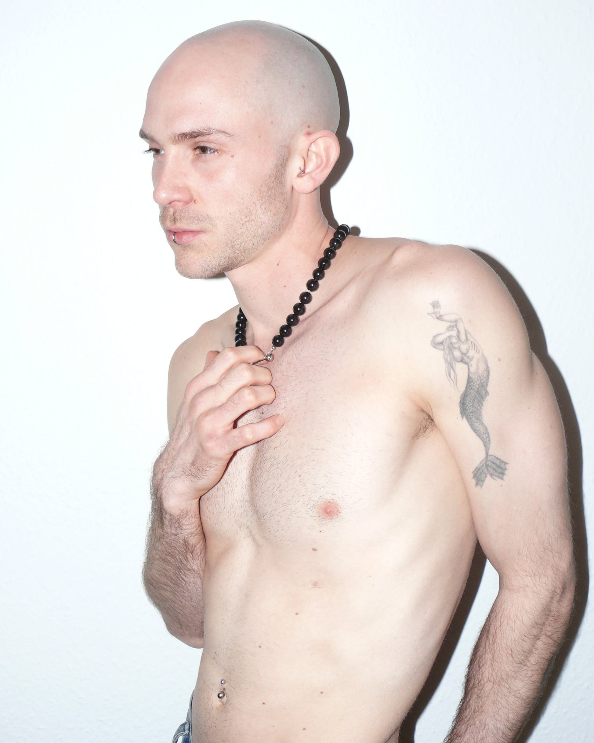 Man with a shaved head and tattoo on his shoulder against a white background