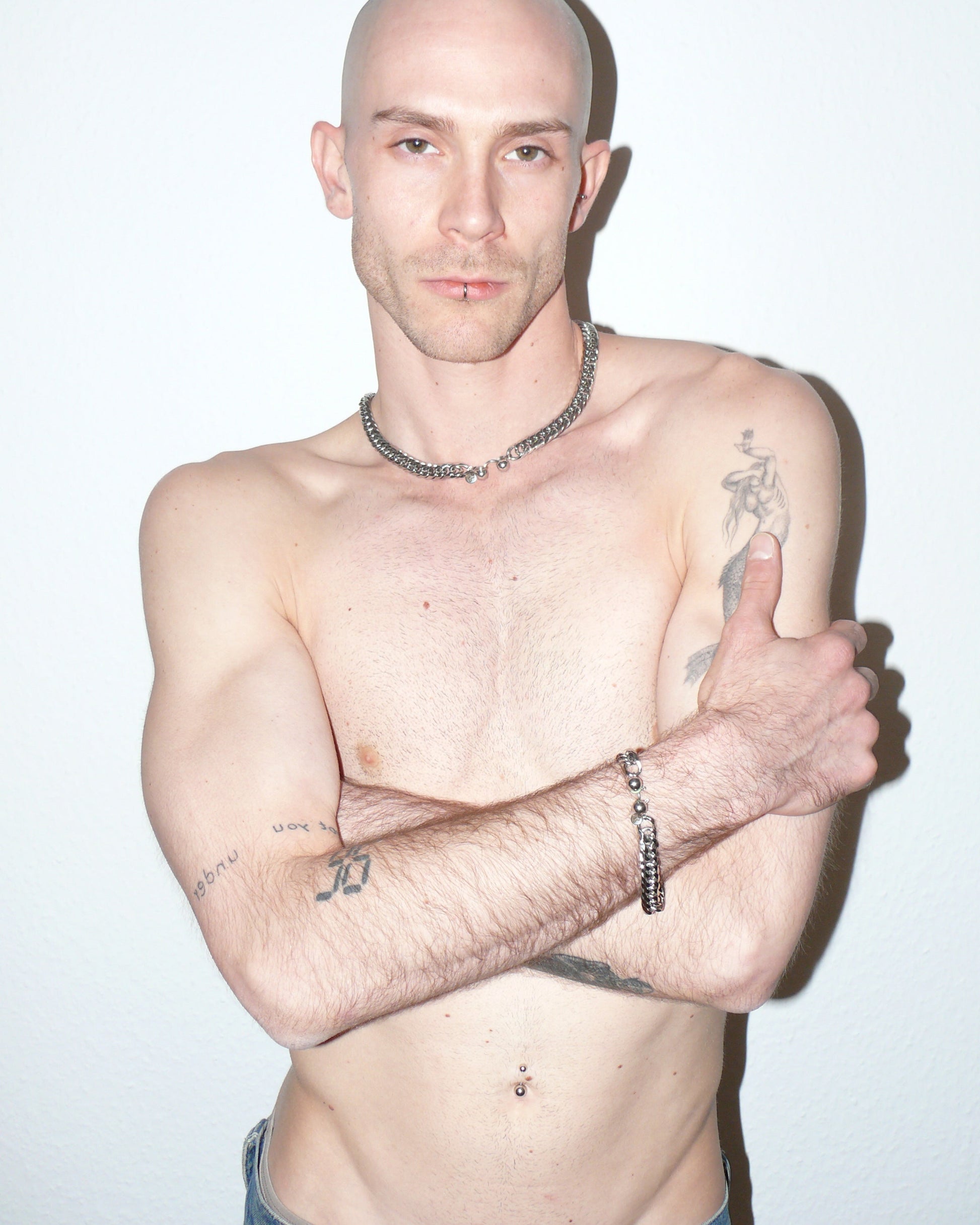 Man with tattoos and jewelry on a plain background