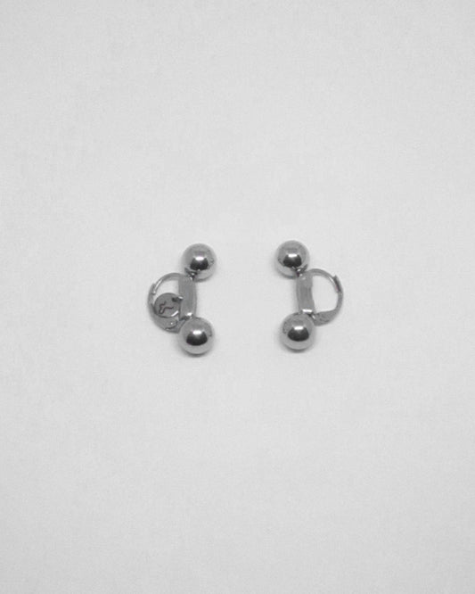 Pair of banana piercing silver earrings on a light gray background