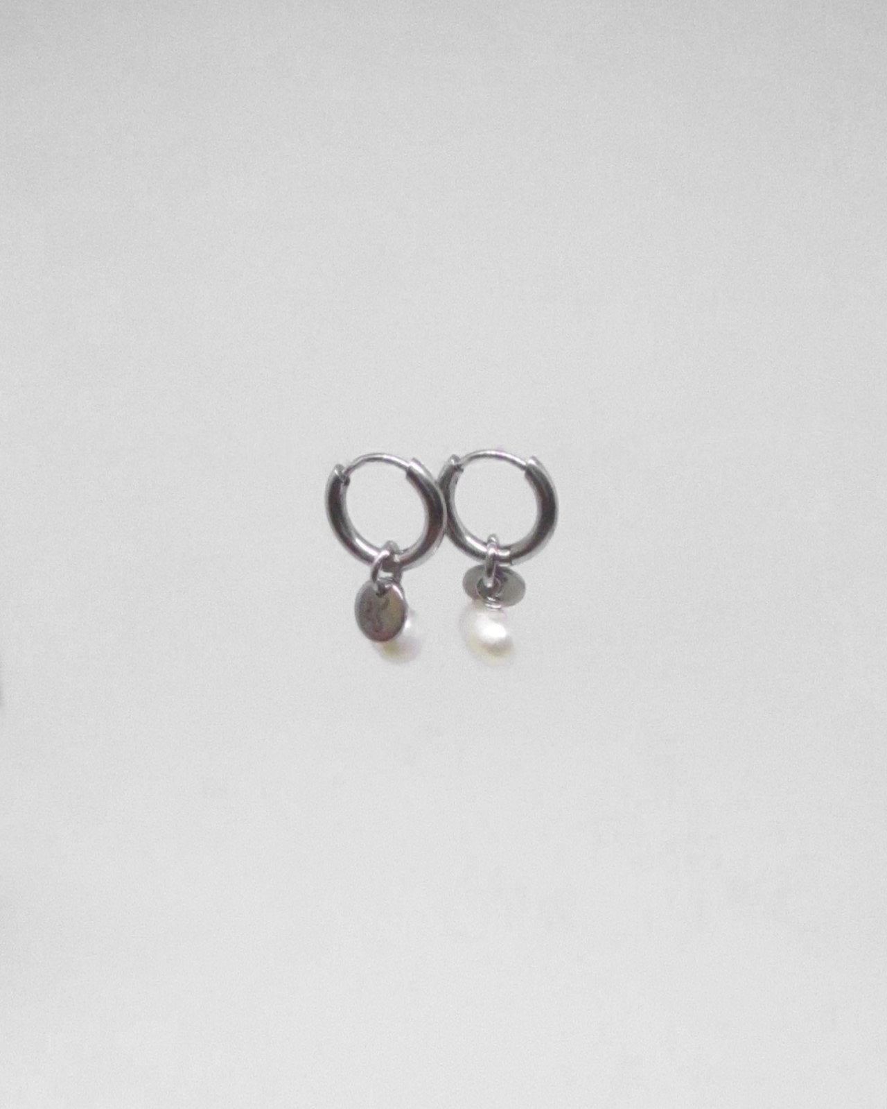 Pair of silver hoop earrings with small round pendants on a light gray background