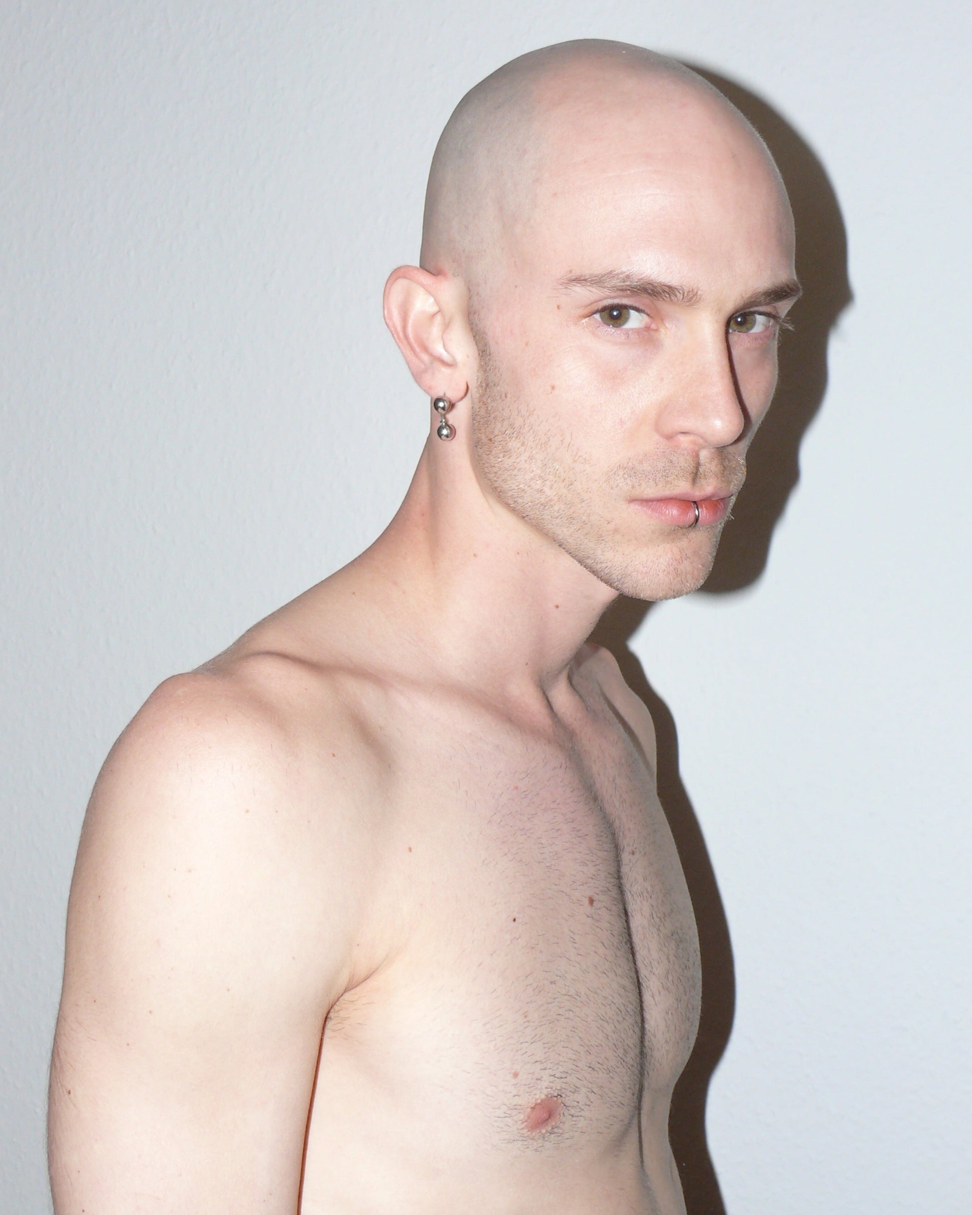 Shirtless man with a shaved head against a plain background