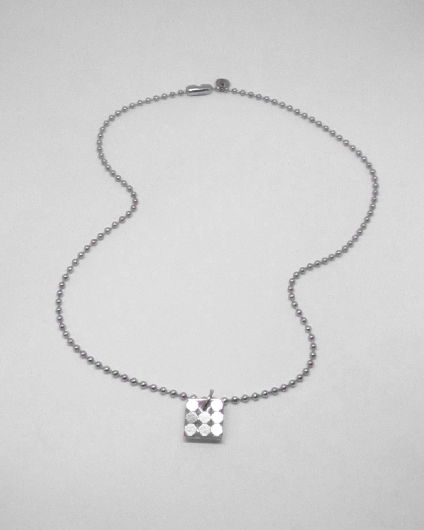 Silver necklace with a square pendant on a light gray background fluid portrait