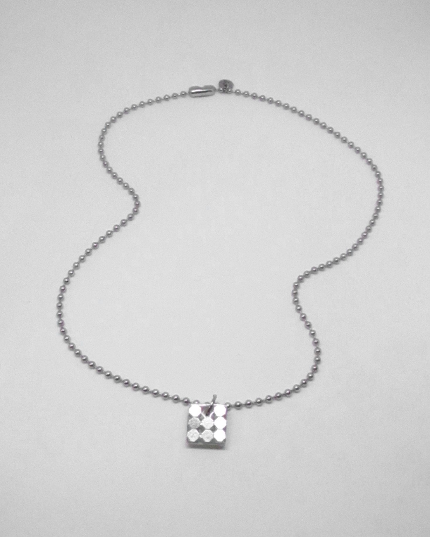 Silver necklace with a square pendant on a light gray background fluid portrait