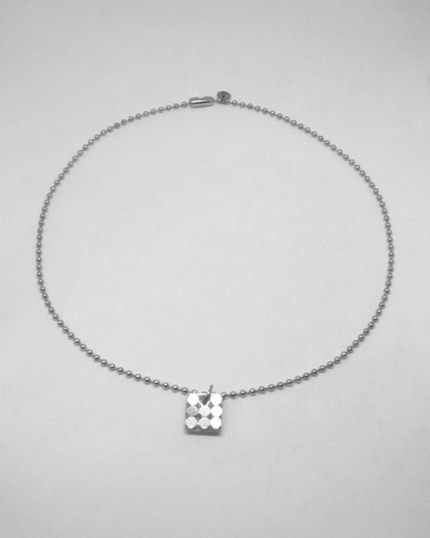 Silver necklace with a square pendant on a light gray background