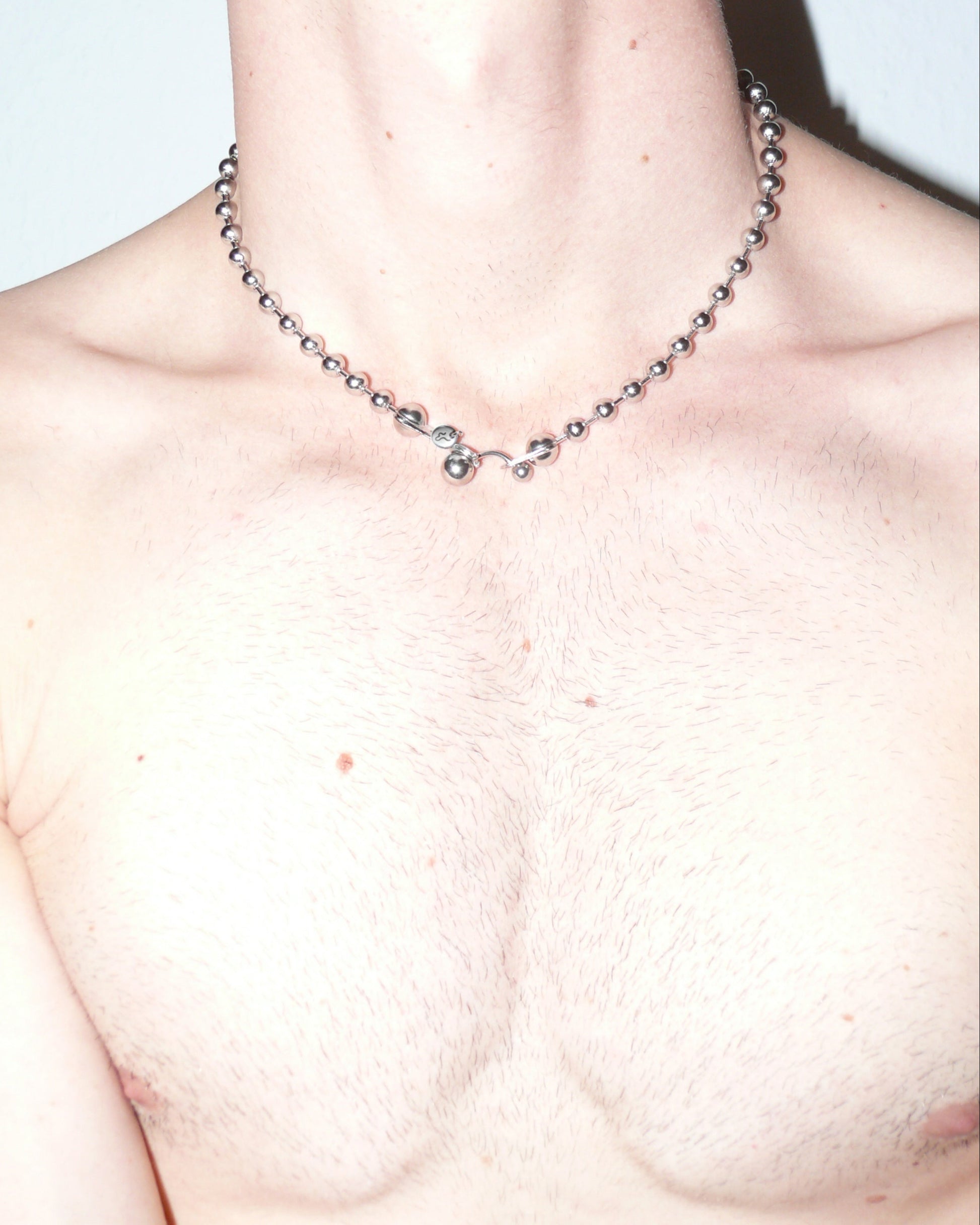 Steel ball chain necklace with piercing closure close up portrait on model torso