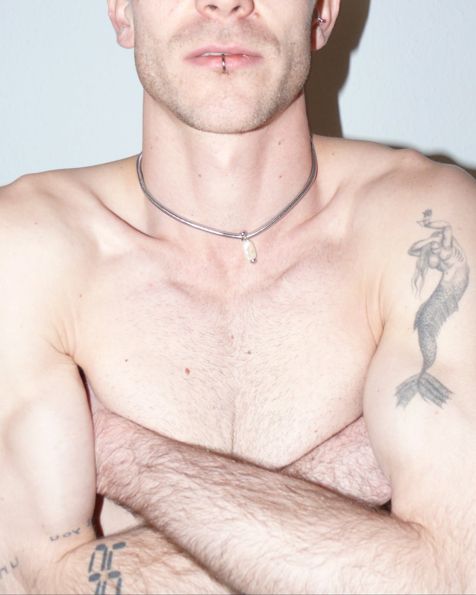 Steel snake chain with pearl pendant decorated with piercing close-up on model with crossed arms on chest