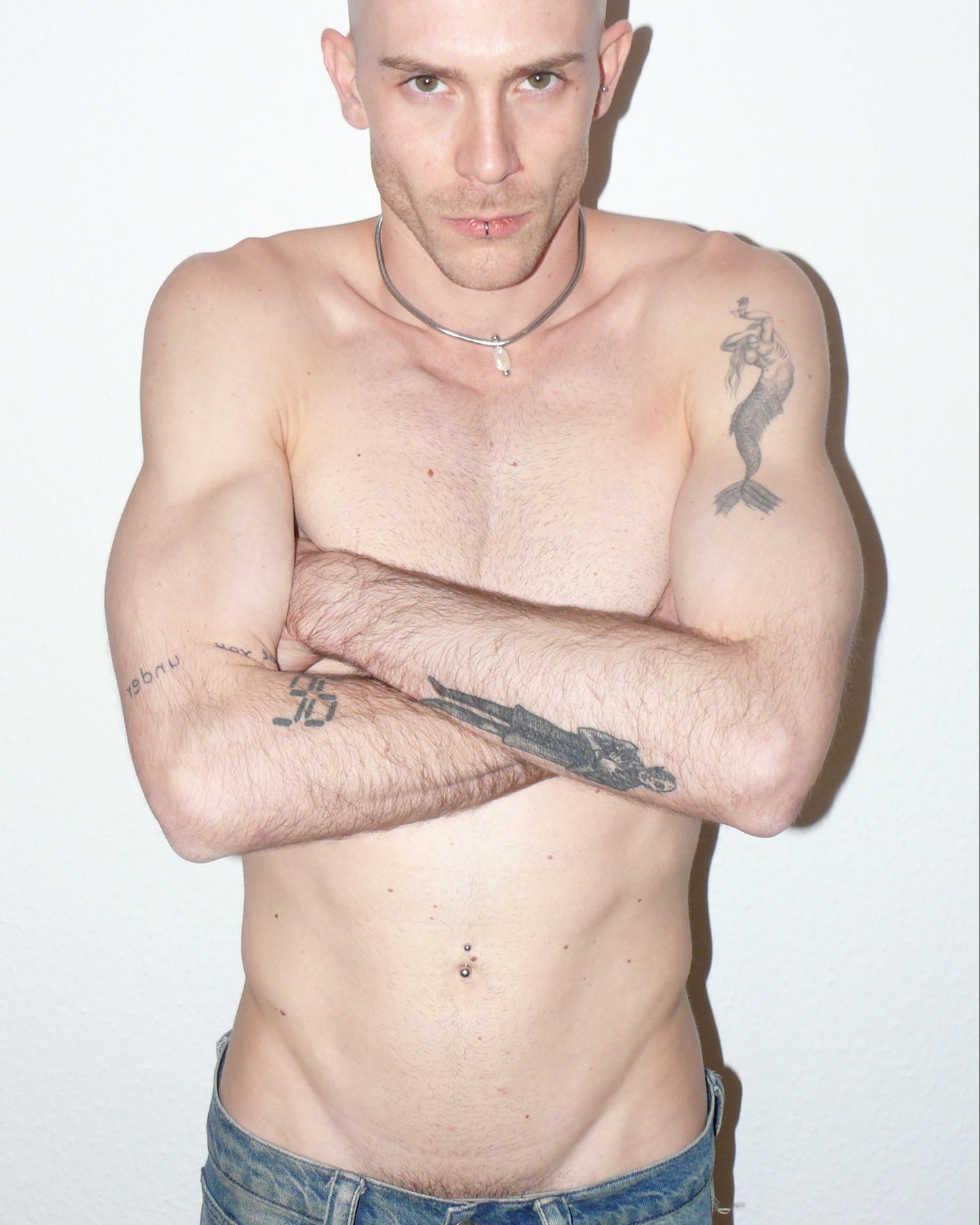 Steel snake chain with pearl pendant decorated with piercing portrait on model with crossed arms on torso