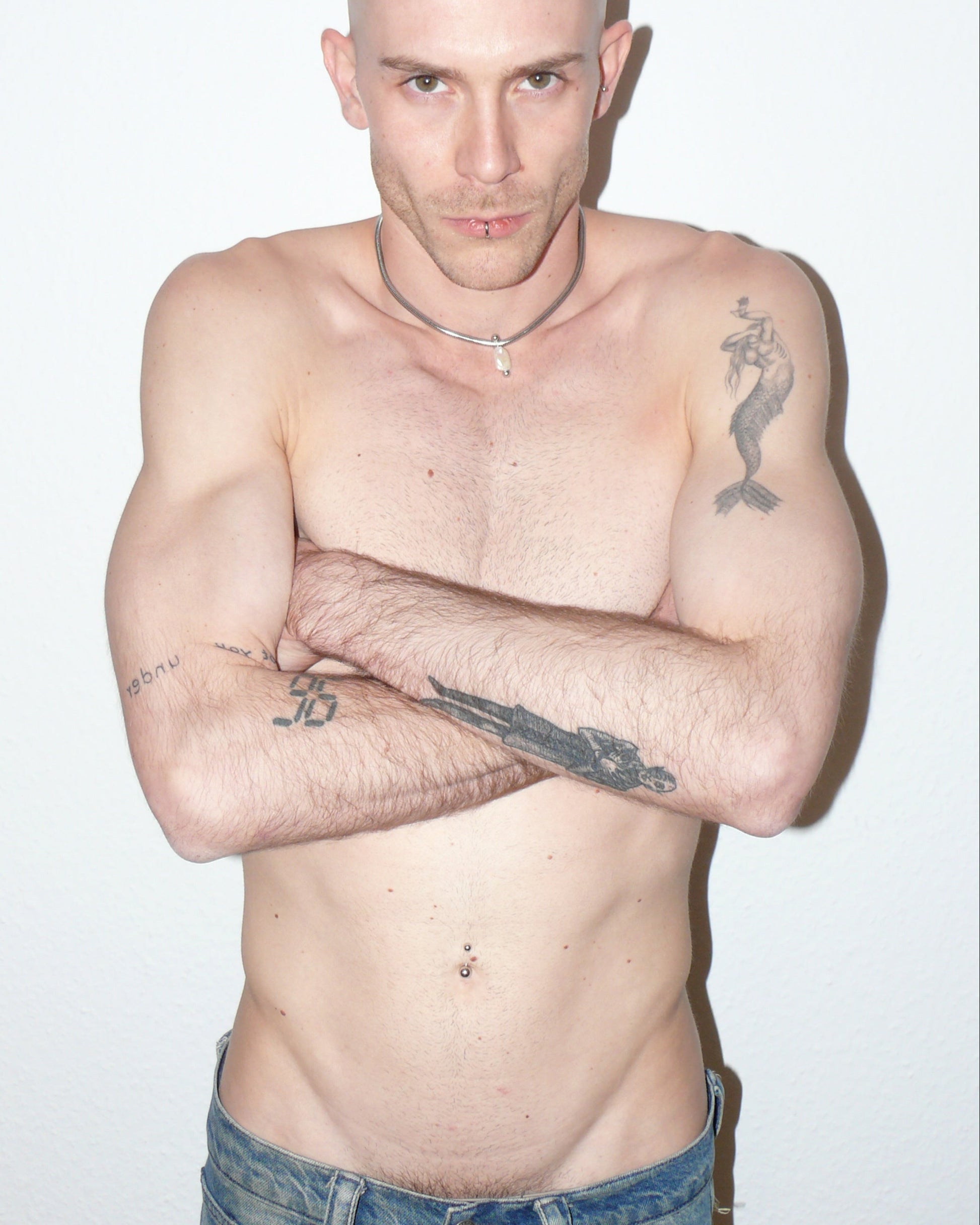 Steel snake chain with pearl pendant decorated with piercing portrait on model with crossed arms on torso